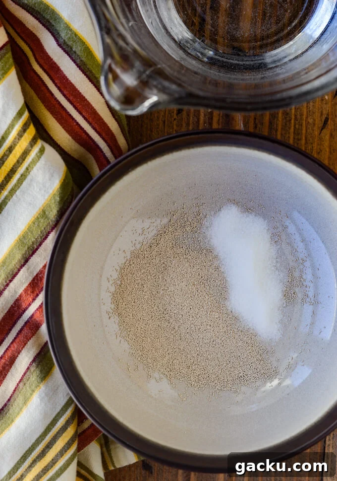 A bowl of yeast with sugar next to a measuring bowl of water and a striped napkin.