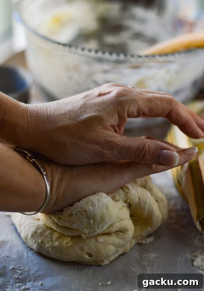 Hands are kneading the pizza dough with a glass bowl in the back.