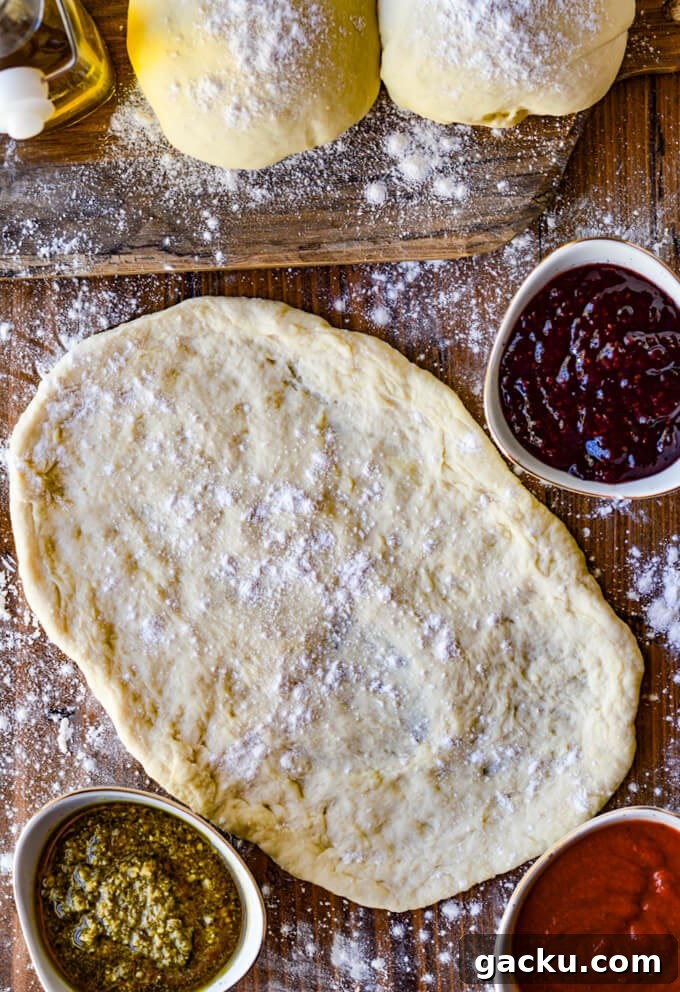 A rolled out pizza dough with two more balls of dough sitting on a wooden board.