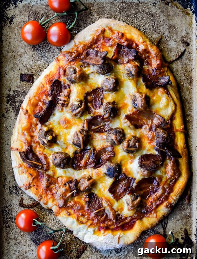 A cooked all-meat pizza on a pizza stone with cherry tomatoes scatter around.