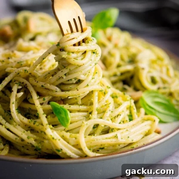 Creamy Baked Gnocchi with Chicken and Parmesan Crisp 10 Square image of pesto spaghetti on a light grey plate being swirled with a gold fork. The pasta is sprinkled with baby basil leaves, toasted pine nuts and parmesan. The plate is on a light grey surface.