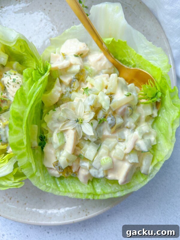 Fluffy Cloud Bread Recipe: Soft, Airy Sandwich Loaf in Minutes 11 A lettuce leaf filled with creamy chicken salad inspired by Olivier Salad, featuring diced chicken, celery, and pickles, garnished with edible flowers and herbs, on a beige plate with a gold spoon.