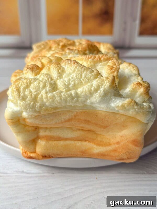 Fluffy Cloud Bread Recipe: Soft, Airy Sandwich Loaf in Minutes 13 A loaf of fluffy, golden-brown bread made using a Cloud Bread Recipe sits on a white plate in front of a window with a warm, softly lit background.