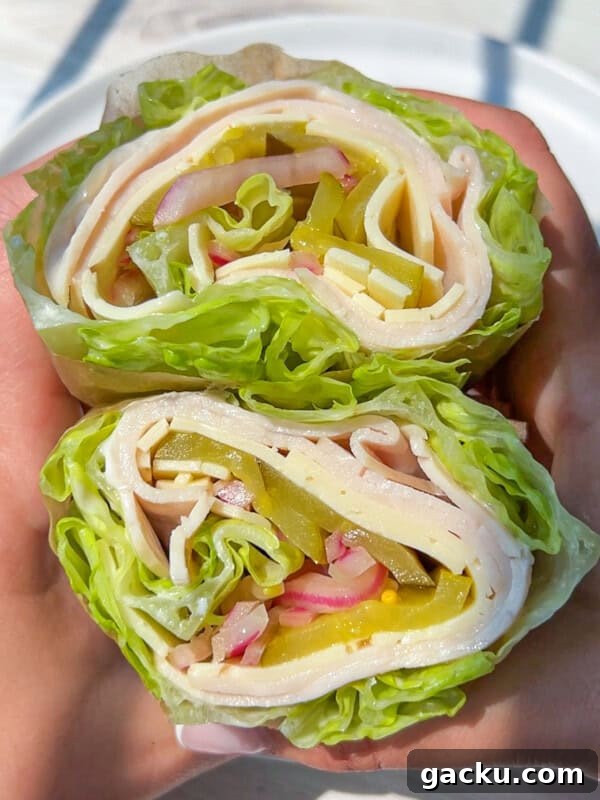 Fluffy Cloud Bread Recipe: Soft, Airy Sandwich Loaf in Minutes 10 Two hands hold lettuce wraps filled with sliced turkey, cheese, pickles, onions, and bell peppers, shown in a close-up view with a white plate in the background.
