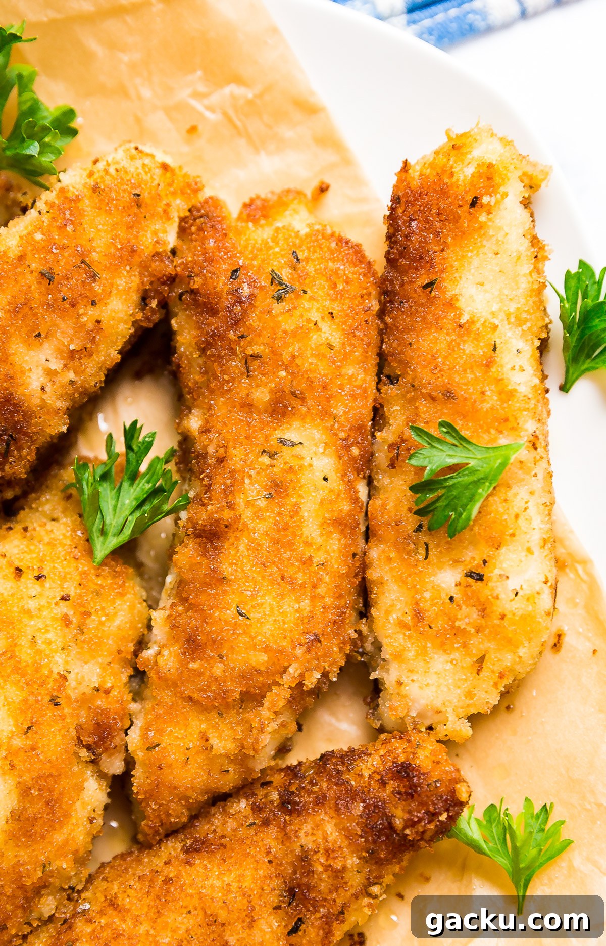 Crispy Pan-Seared Chicken Cutlets with Lemon Garlic Sauce 2 A close up of chicken cutlets laid next to each other on parchment with a couple sprigs of parsley.