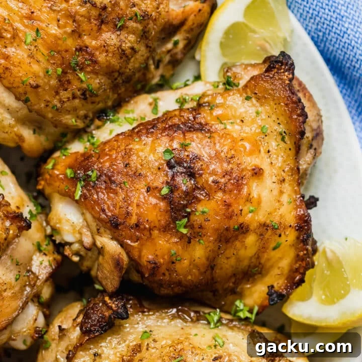 A close up overhead image of grilled chicken thighs on a plate with lemons.
