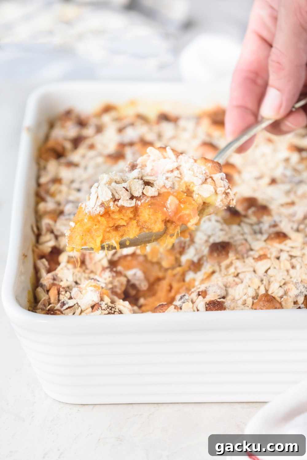 Someone is scooping sweet potato casserole out of a white casserole dish with a spoon.