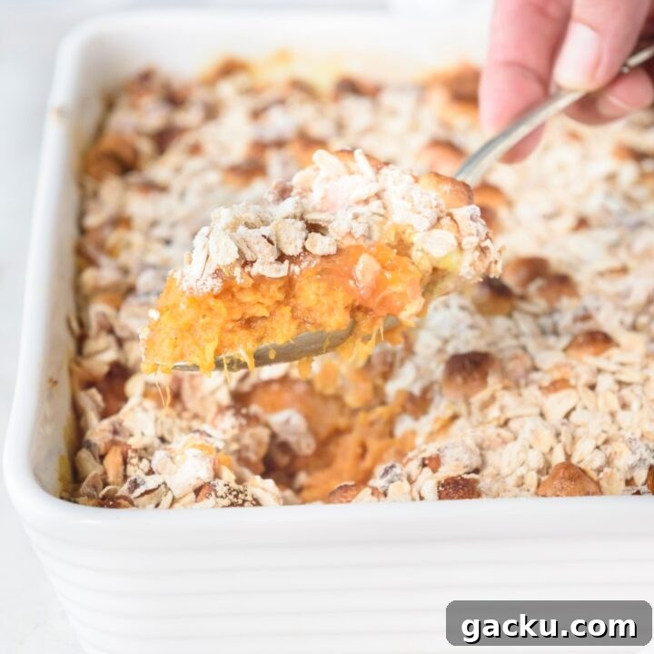Someone is scooping sweet potato casserole out of a white casserole dish with a spoon.