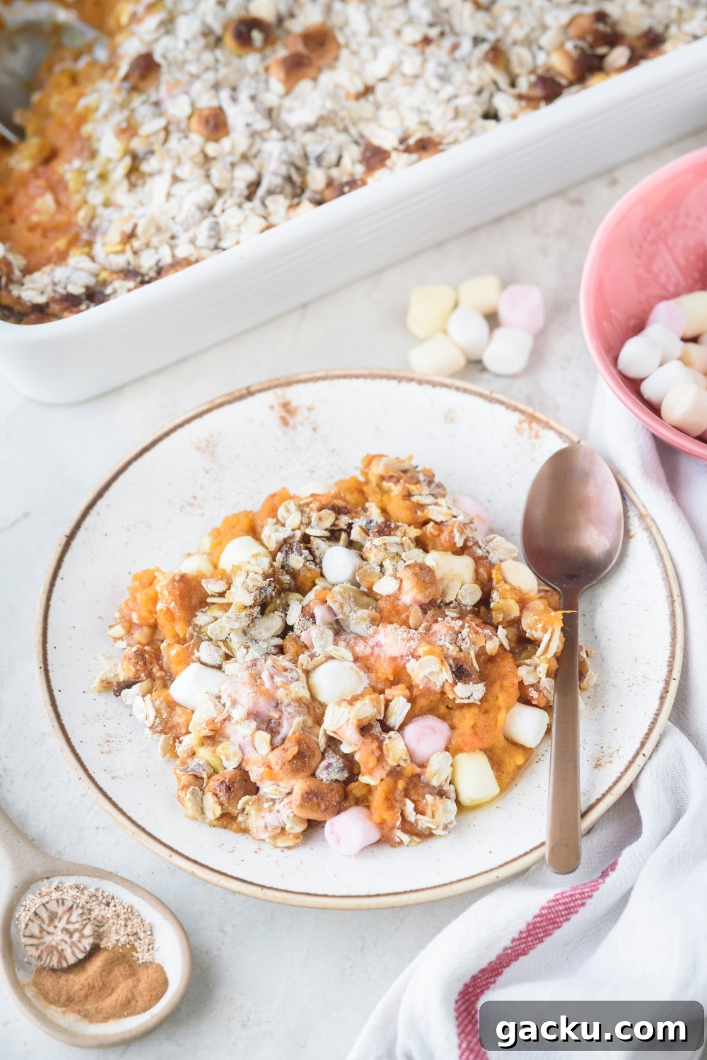 A white plate full of sweet potato casserole on a white counter. A spoon rests on the plate.