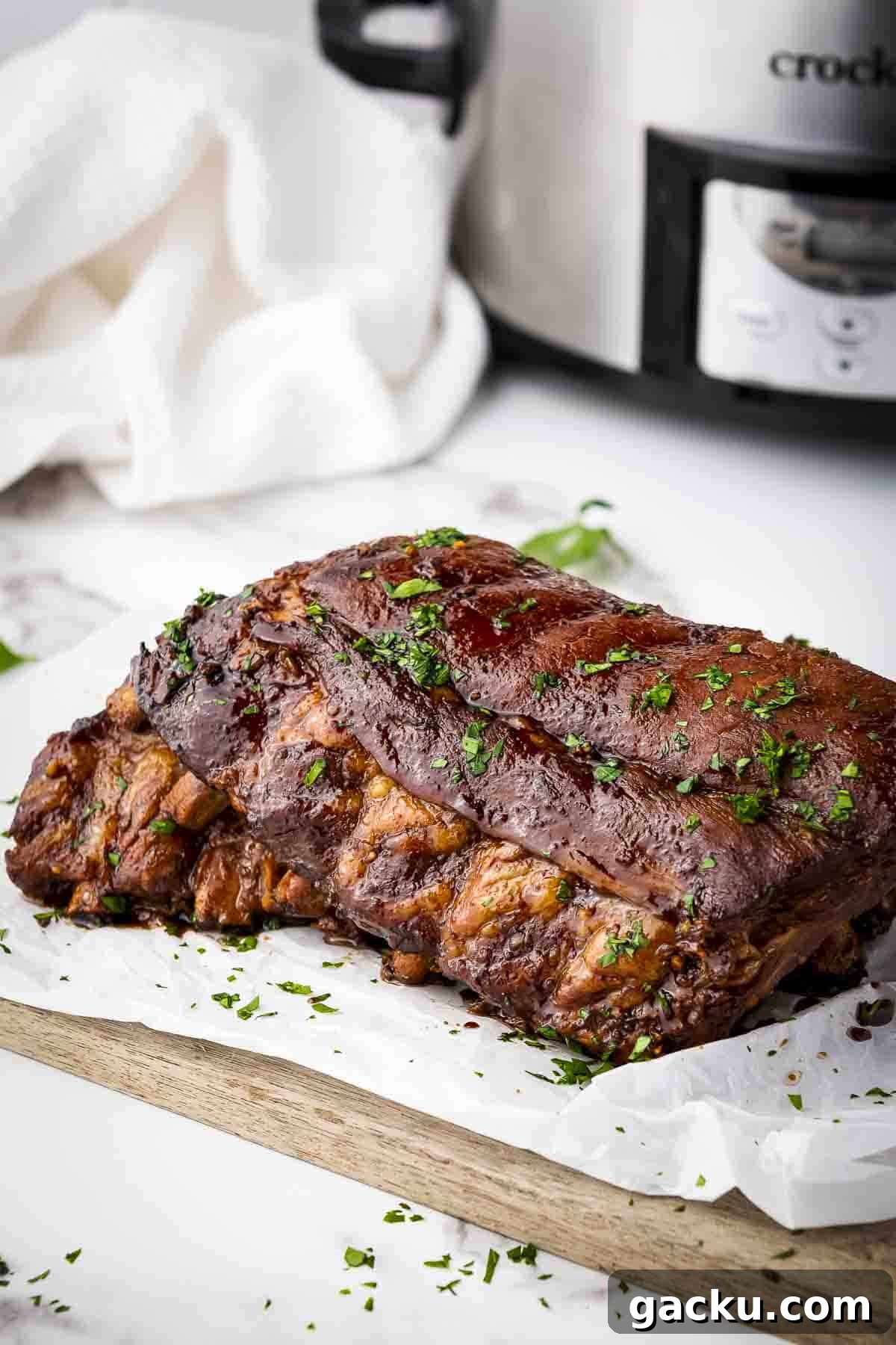 Slow-Cooked Honey Garlic Ribs with Sticky Glaze 2 Side shot of multiple ribs garnished with parsely on a piece of butcher paper on a wooden cutting board.
