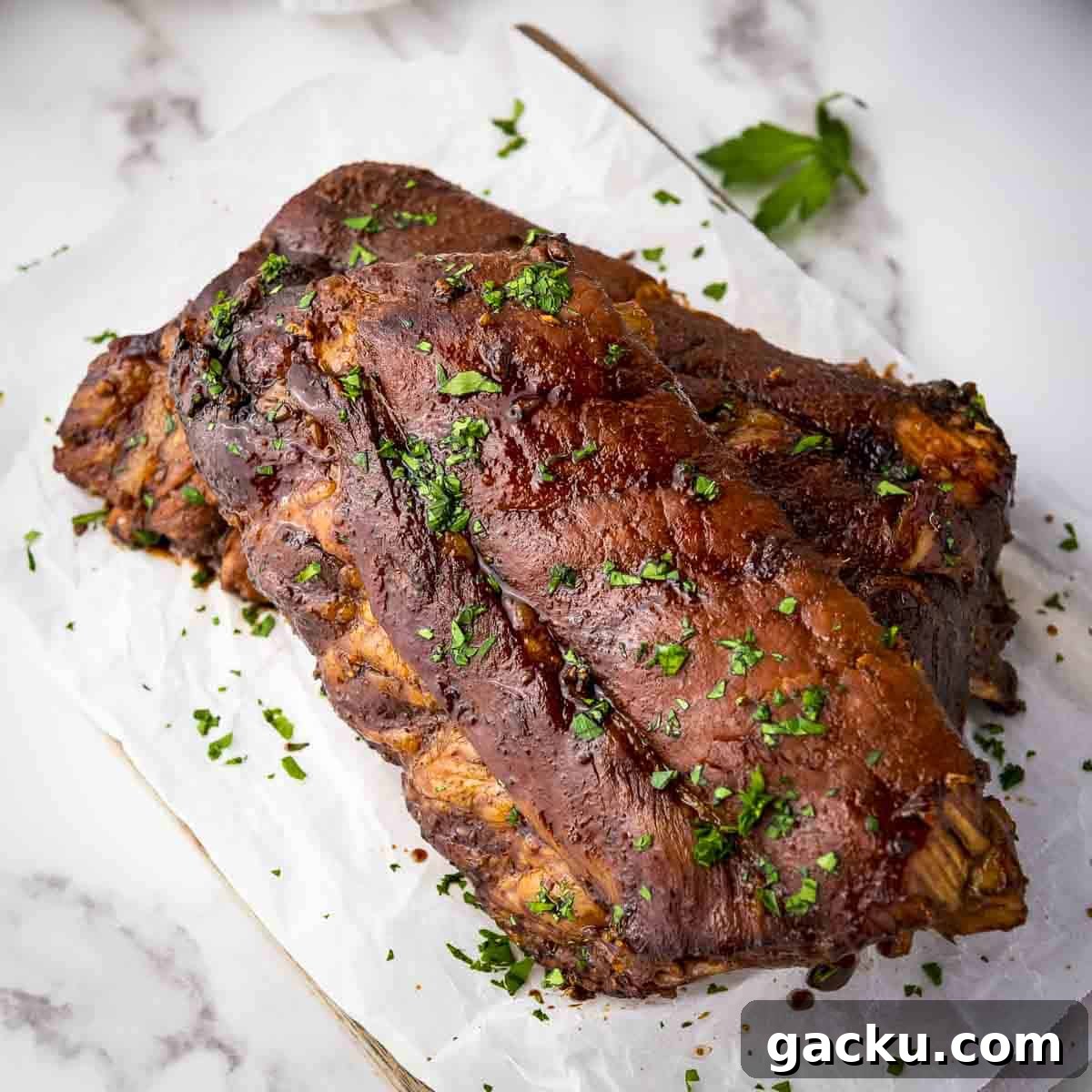 Slow-Cooked Honey Garlic Ribs with Sticky Glaze 7 Overhead shot of multiple ribs garnished with parsely on a piece of butcher paper on a wooden cutting board.