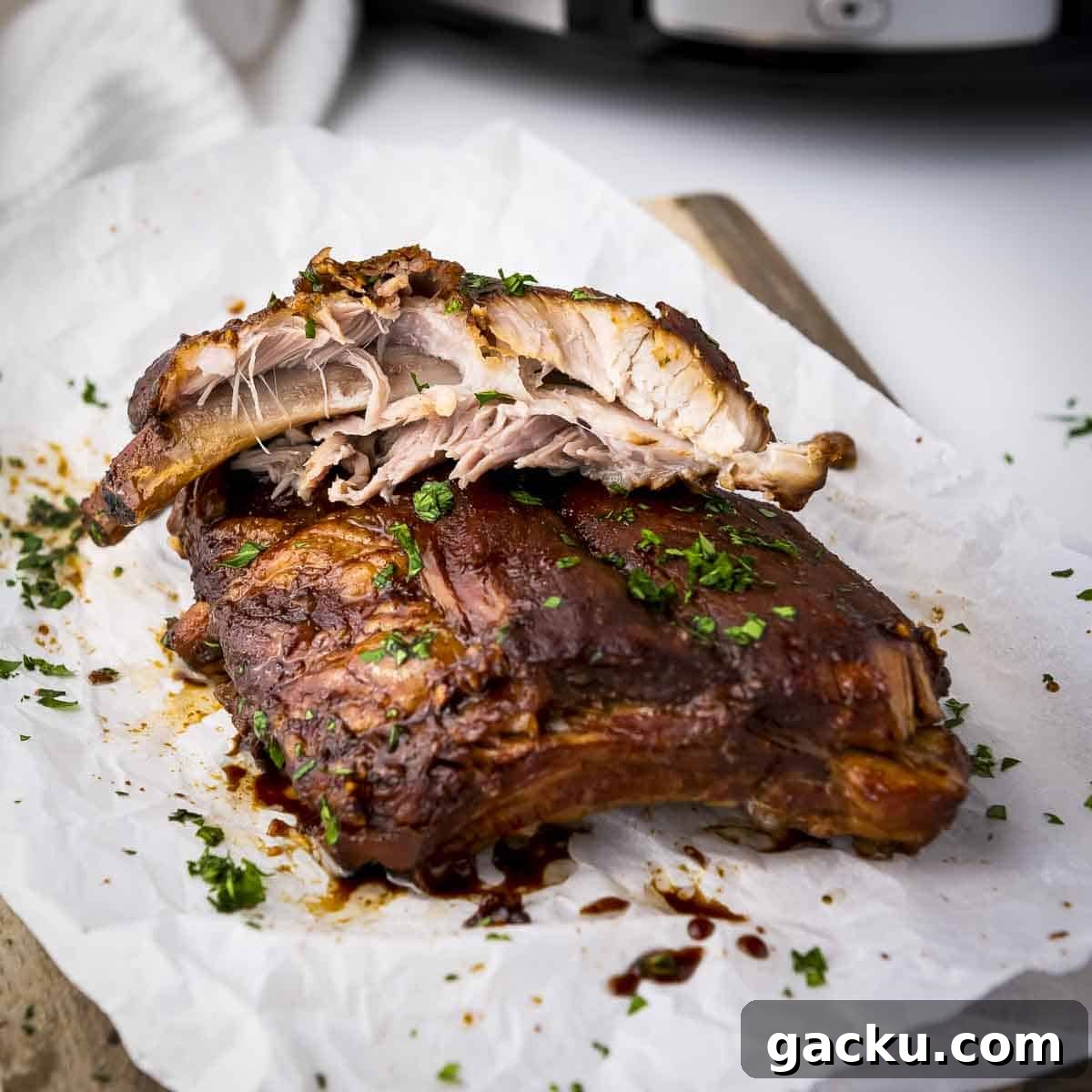 Slow-Cooked Honey Garlic Ribs with Sticky Glaze 8 Side shot of multiple ribs garnished with parsely on a piece of butcher paper on a wooden cutting board.