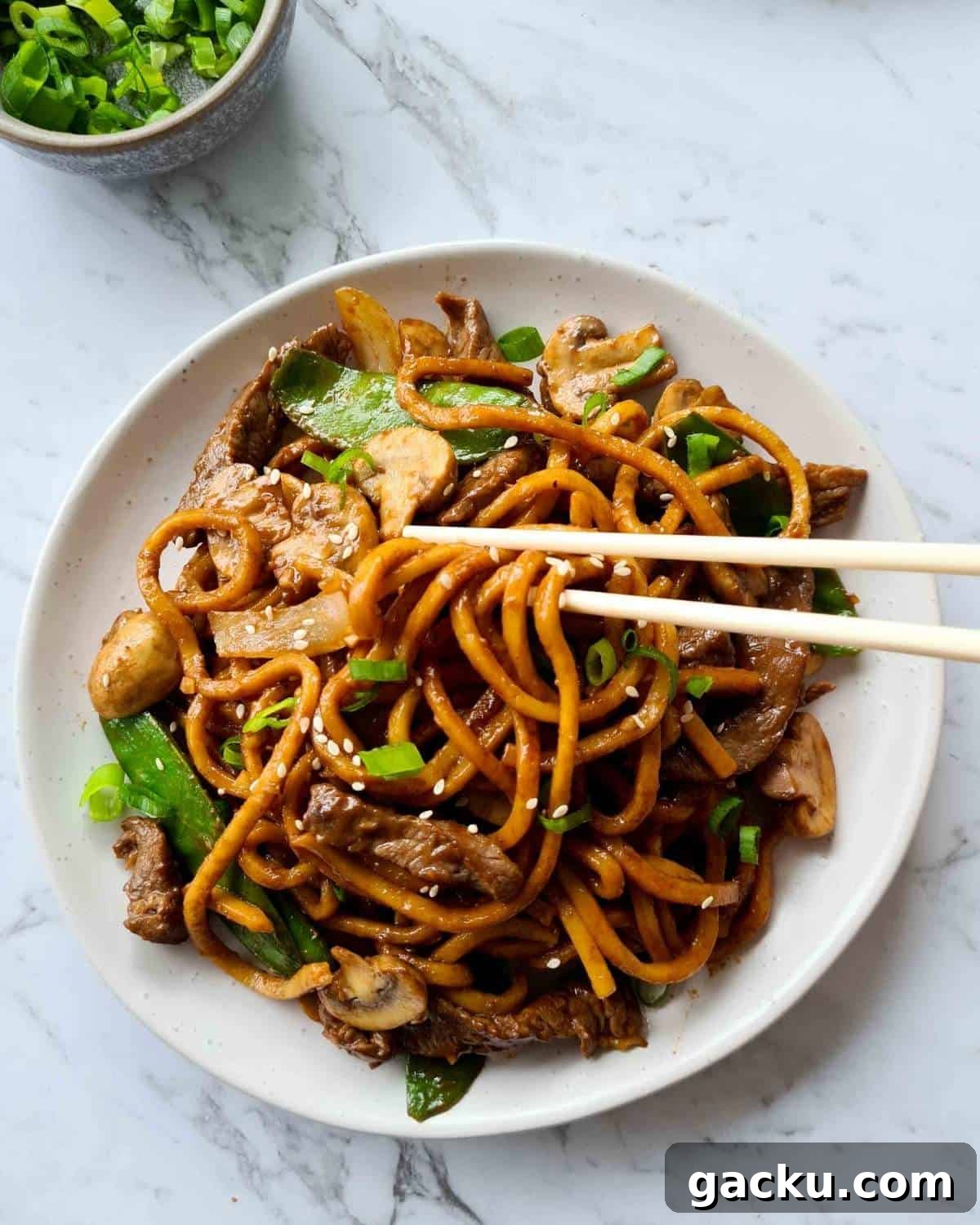 Szechuan Beef Stir-Fry with Noodles: Quick Weeknight Recipe 13 Cooked noodle stir fry in a white plate with a pair of chopsticks