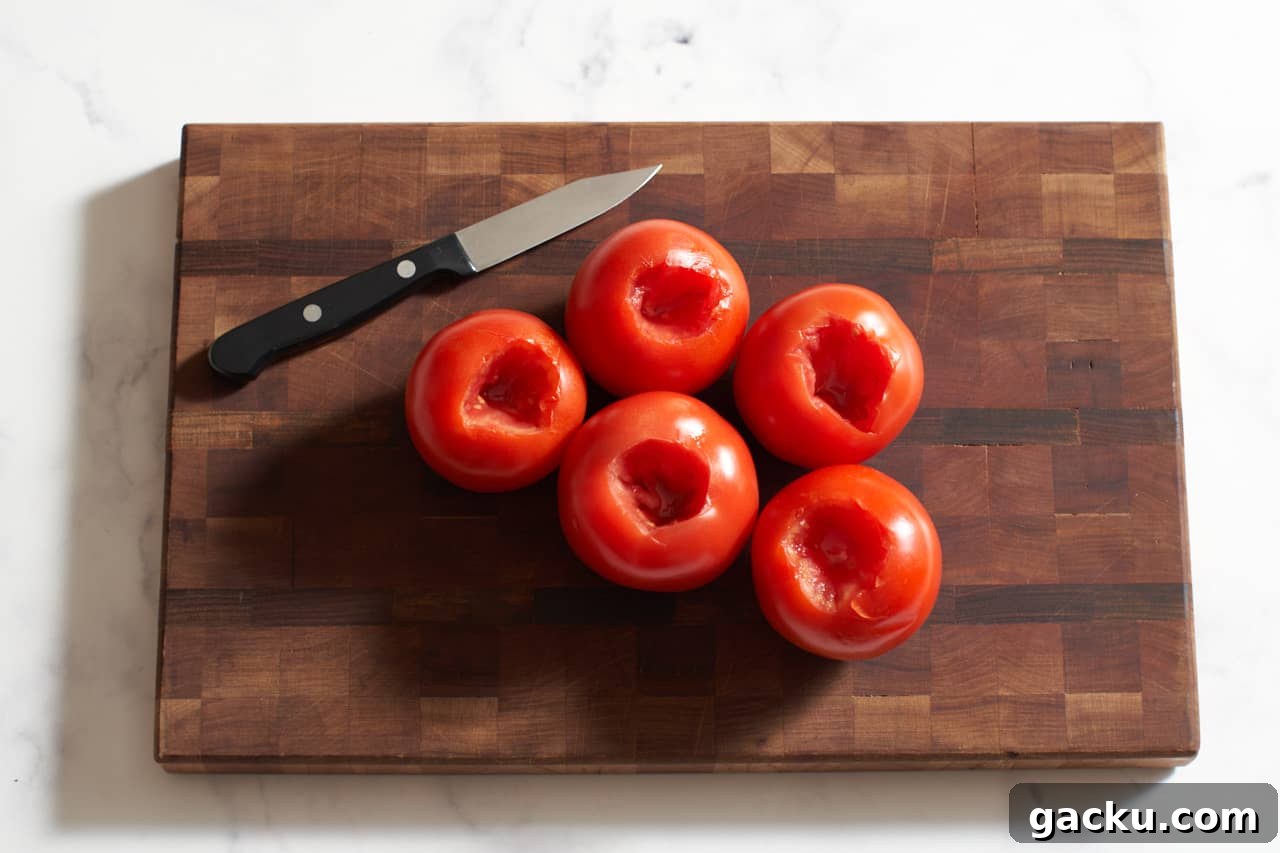 A paring knife on a wooden cutting board next to five tomatoes that have been cored.