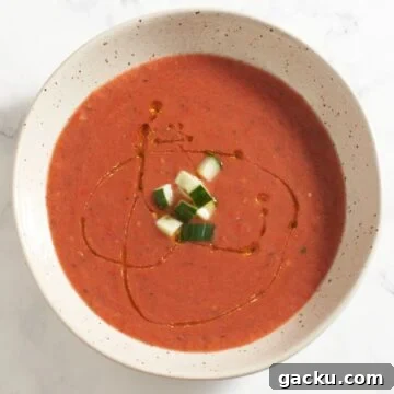 Top down view of a bowl of gazpacho topped with chopped cucumber and a drizzle of olive oil.