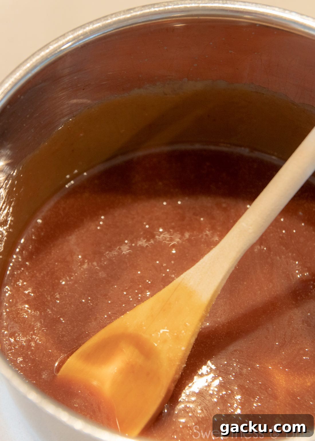 A saucepan with caramel sauce in it, with a wooden spoon.