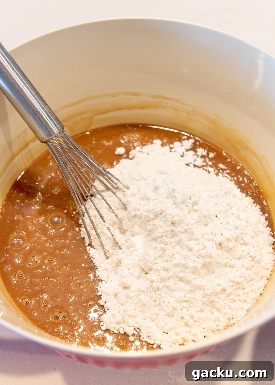 Large bowl with caramel mud cake batter and a balloon whisk. 