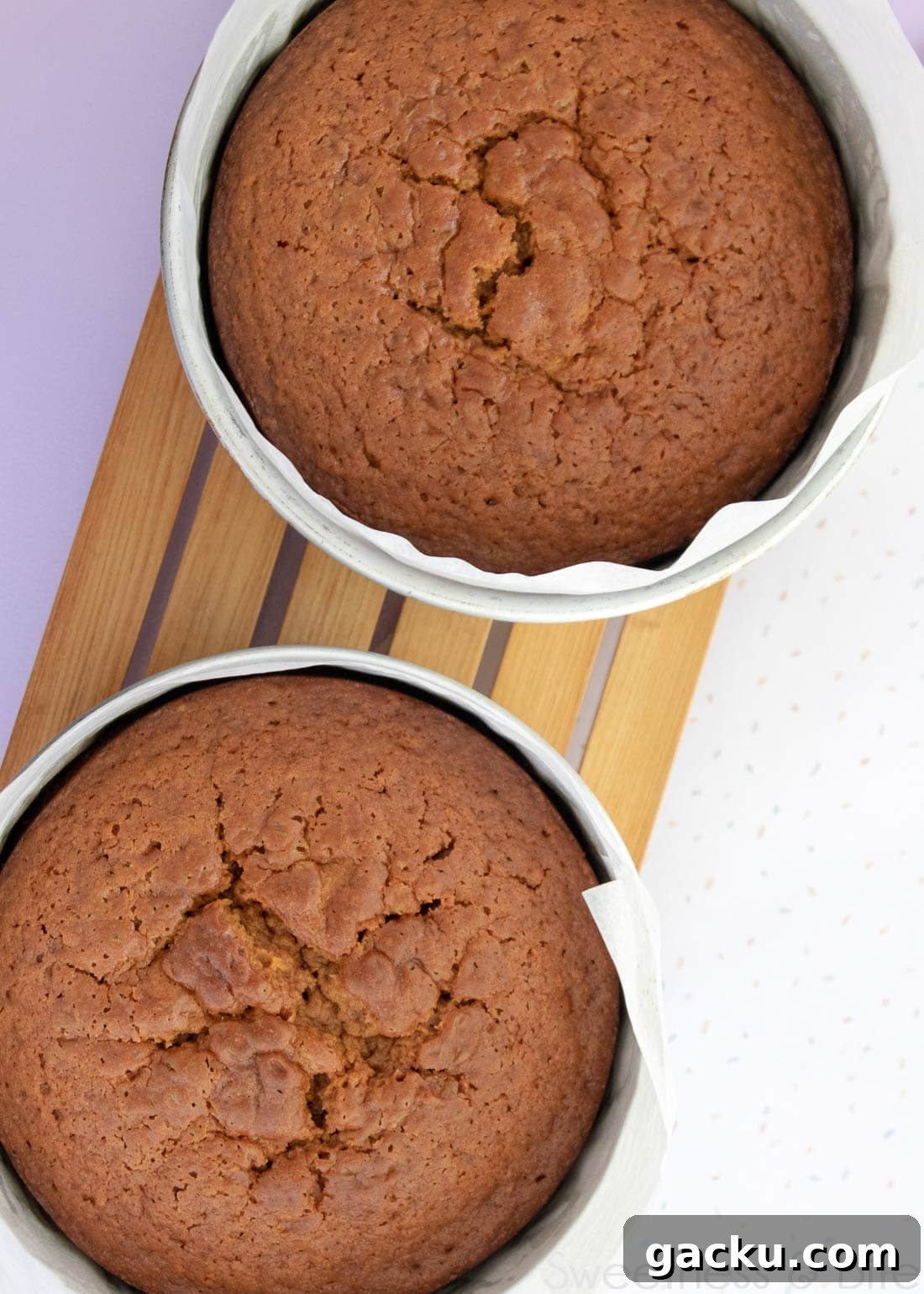 Two cakes in cake pans on a wooden cooling rack.