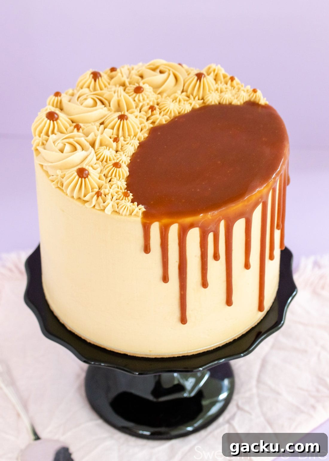 Caramel mud cake on a black cake stand, decorated with swirls of caramel buttercream on top, and a caramel sauce drip. 
