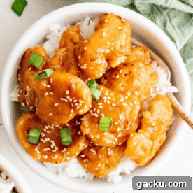 A bowl of chicken breast sesame chicken served over white rice, garnished with green onions and sesame seeds.
