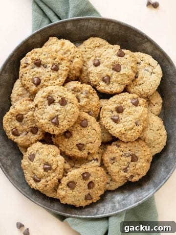 Close up of metal plate with piled chocolate chip oatmeal cookies. Green cloth beneath it. Light peach surface.