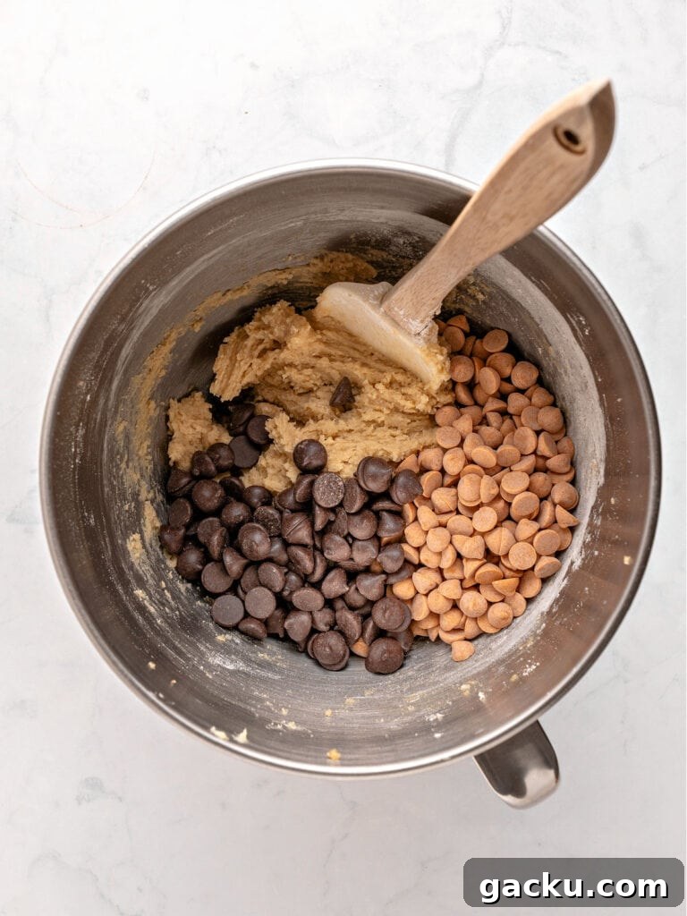 Chewy Butterscotch Chocolate Chip Cookies — No-Chill Dough Recipe 6 Metal bowl with chocolate and butterscotch chips with cookie dough. Wooden spatula. Light gray background.