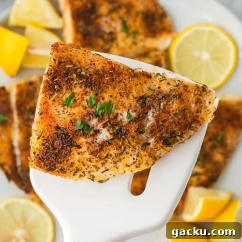 Juicy, seasoned grilled fish fillet with lemon wedges on a white serving spatula.