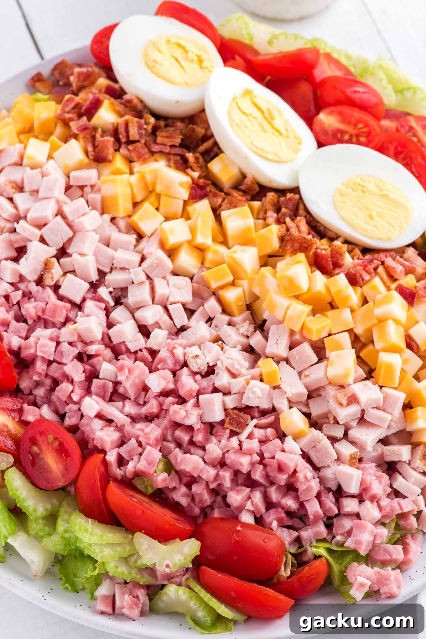 A close up of the rows of toppings on a Chef salad in a white bowl.