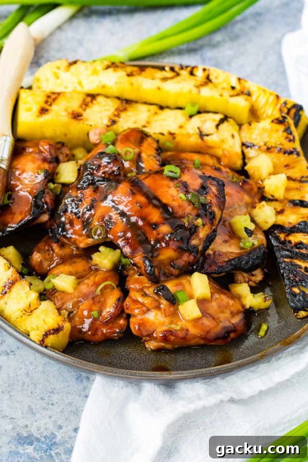 A photo of grilled huli huli chicken with grilled pineapple in the background.