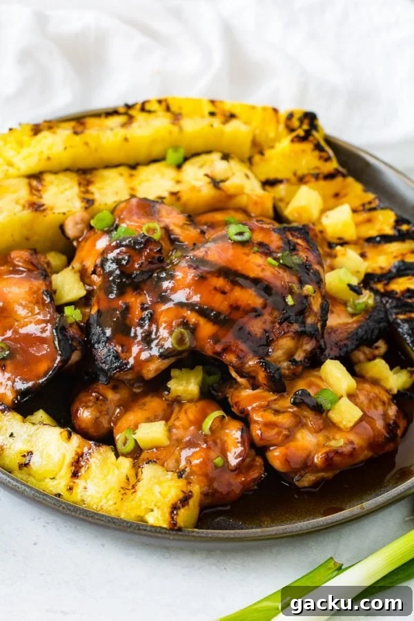 A photo of grilled huli huli chicken with grilled pineapple in the background.
