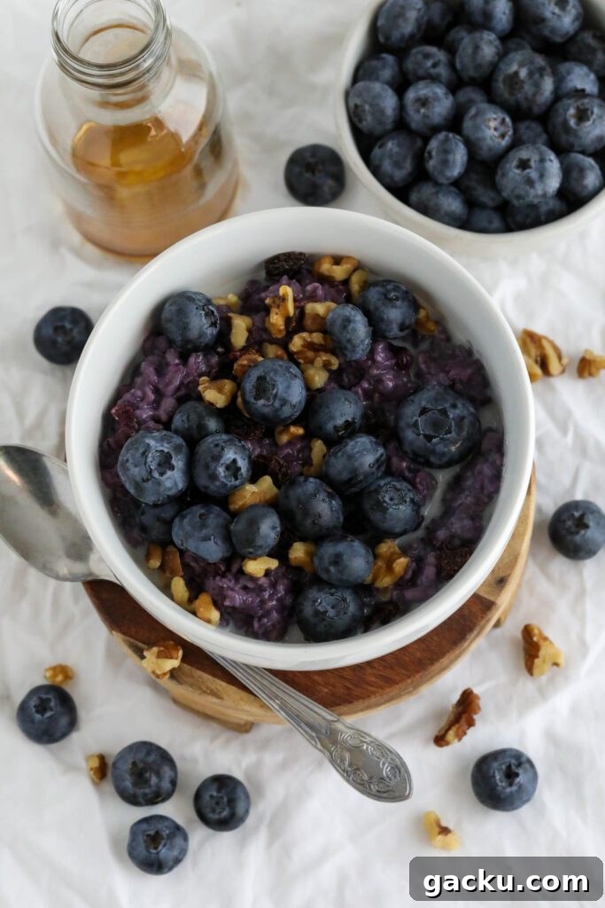 Creamy Blueberry Oatmeal Made on the Stovetop 2 Blueberry Stovetop Oatmeal served on wooden pedestal with scattered blueberries and walnuts with spoon