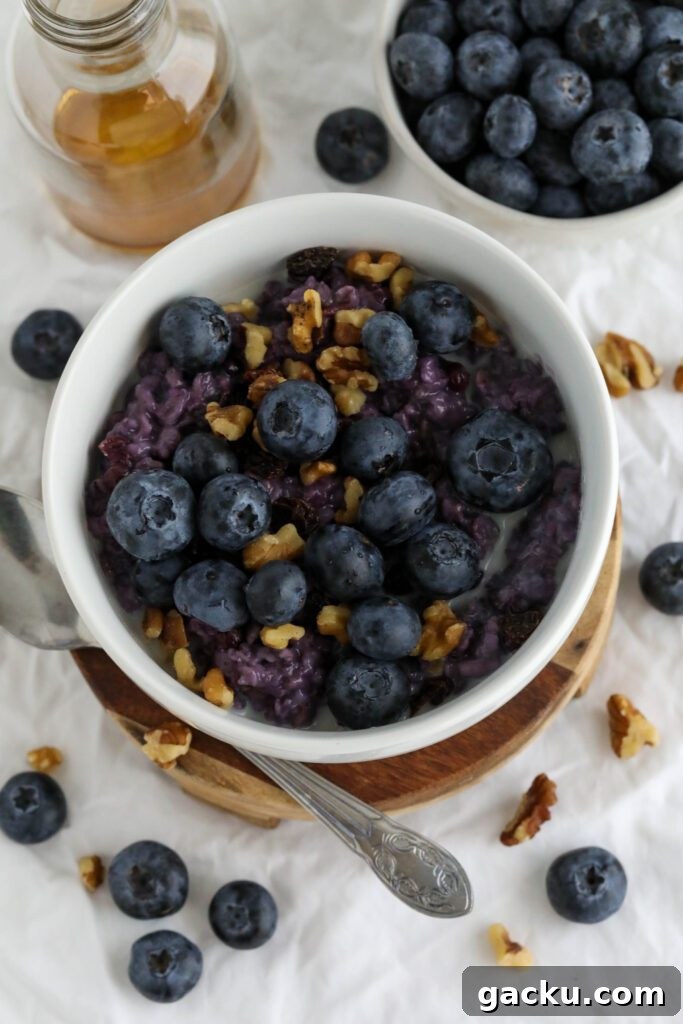 Creamy Blueberry Oatmeal Made on the Stovetop 7 Blueberry Stovetop Oatmeal served on wooden pedestal with scattered blueberries and walnuts with spoon