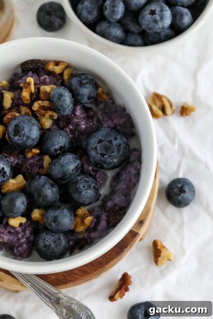 Creamy Blueberry Oatmeal Made on the Stovetop 8 Blueberry Stovetop Oatmeal served on wooden pedestal with scattered blueberries and walnuts with spoon