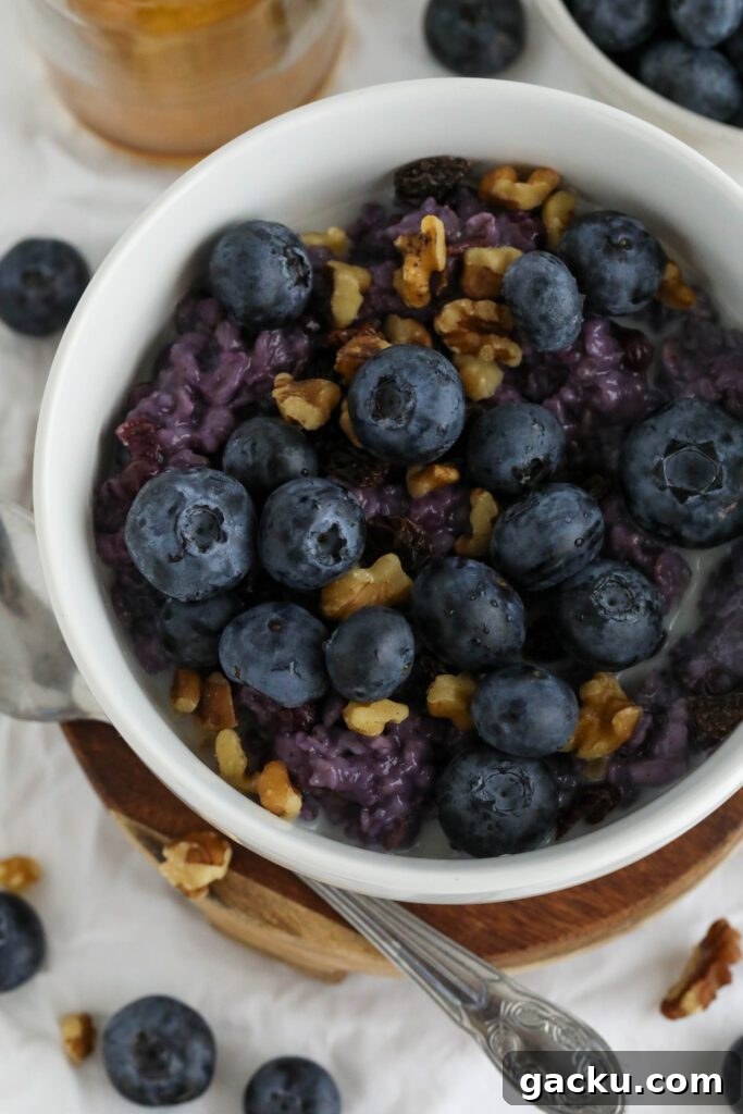 Creamy Blueberry Oatmeal Made on the Stovetop 9 Blueberry Stovetop Oatmeal served on wooden pedestal with scattered blueberries and walnuts with spoon