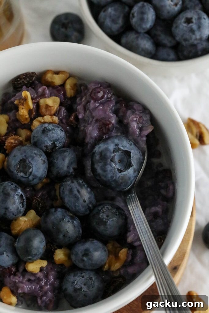 Creamy Blueberry Oatmeal Made on the Stovetop 10 Blueberry Stovetop Oatmeal served on wooden pedestal with scattered blueberries and walnuts with spoon