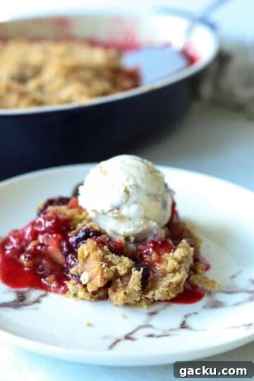 plate with slice of apple blackberry crumble topped with butter pecan ice cream