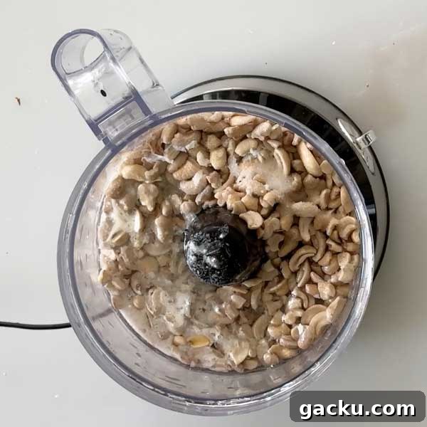 Adding soaked cashews to the cream cheese filling ingredients in a food processor.