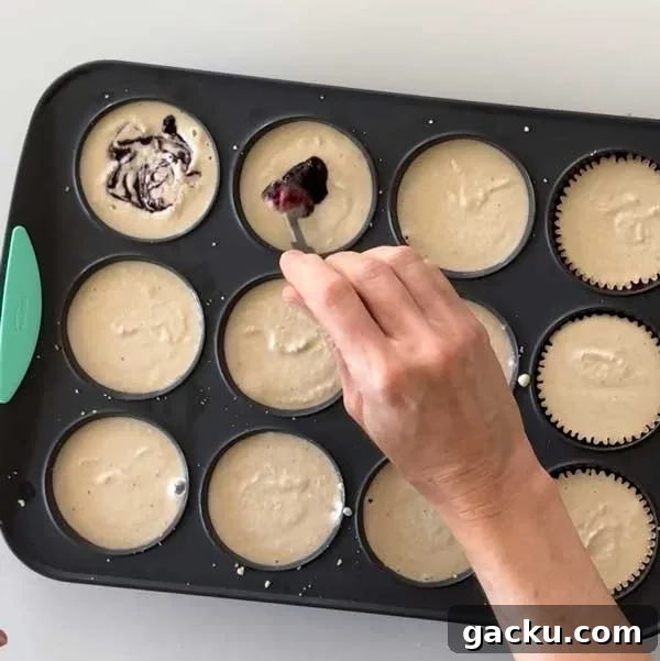 Adding blueberry sauce to the cheesecakes in the muffin pan.