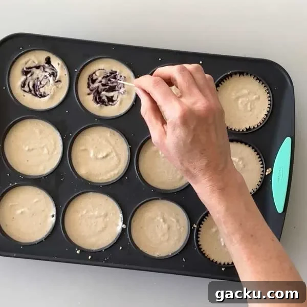 Using a toothpick to swirl blueberry sauce into the cheesecake filling in a muffin pan.