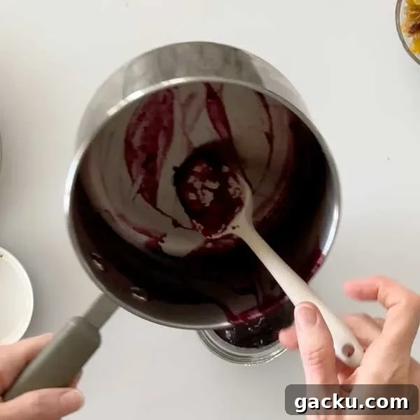 Transferring blueberry sauce from the sauce pan to a bowl with a spatula.
