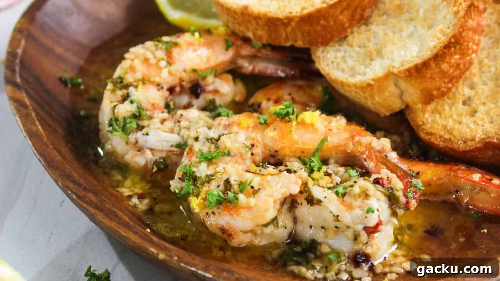 30 One-Pan Skillet Meals for Quick Cleanup and Big Flavor 3 Cooked shrimp in a garlic butter sauce, garnished with chopped parsley, served in a wooden bowl alongside slices of toasted bread and a lemon wedge.