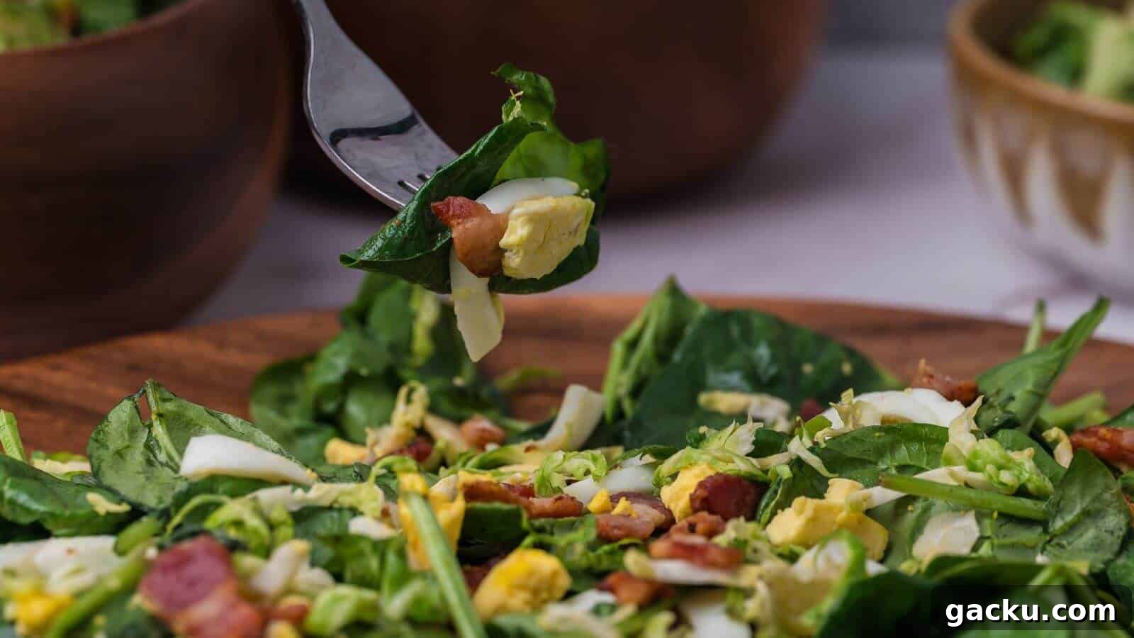 30 One-Pan Skillet Meals for Quick Cleanup and Big Flavor 22 A fork holds a bite of spinach salad with chopped eggs, bacon, and cheese over a wooden bowl filled with the same salad. Two blurred bowls are in the background.