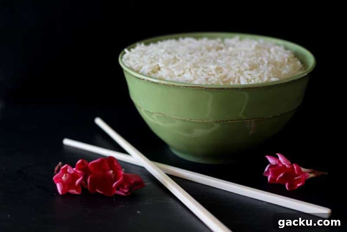 Simple Rice Pilaf Recipe: Fluffy, Flavorful Rice Pilaf in 30 Minutes 10 Green bowl sitting on a black table containing white rice, crossed chopsticks and 3 red flowers on table.