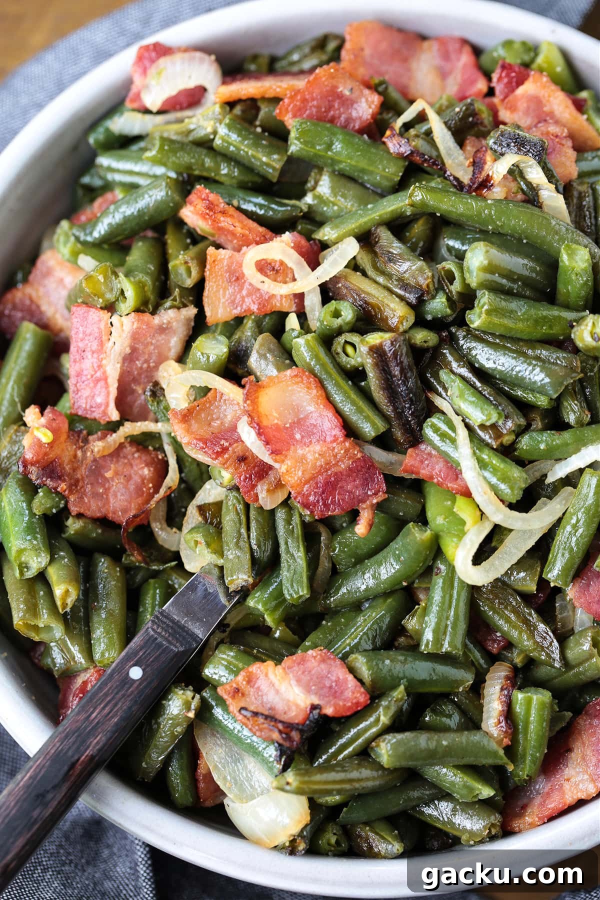 Cook: Place the sheet pan in the oven and cook for 20 minutes, toss and cook for another 20 minutes until the onions are soft and the green beans have color. green beans with bacon and onions in bowl with spoon