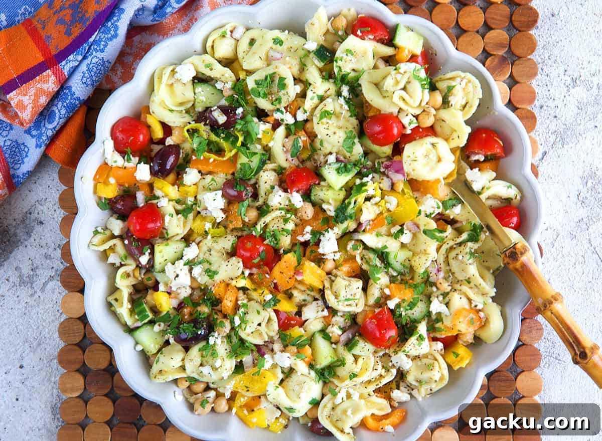 Greek Tortellini Salad with Feta, Olives & Lemon Dressing 2 Greek Tortellini Pasta Salad in a white serving bowl with a bamboo serving spoon.