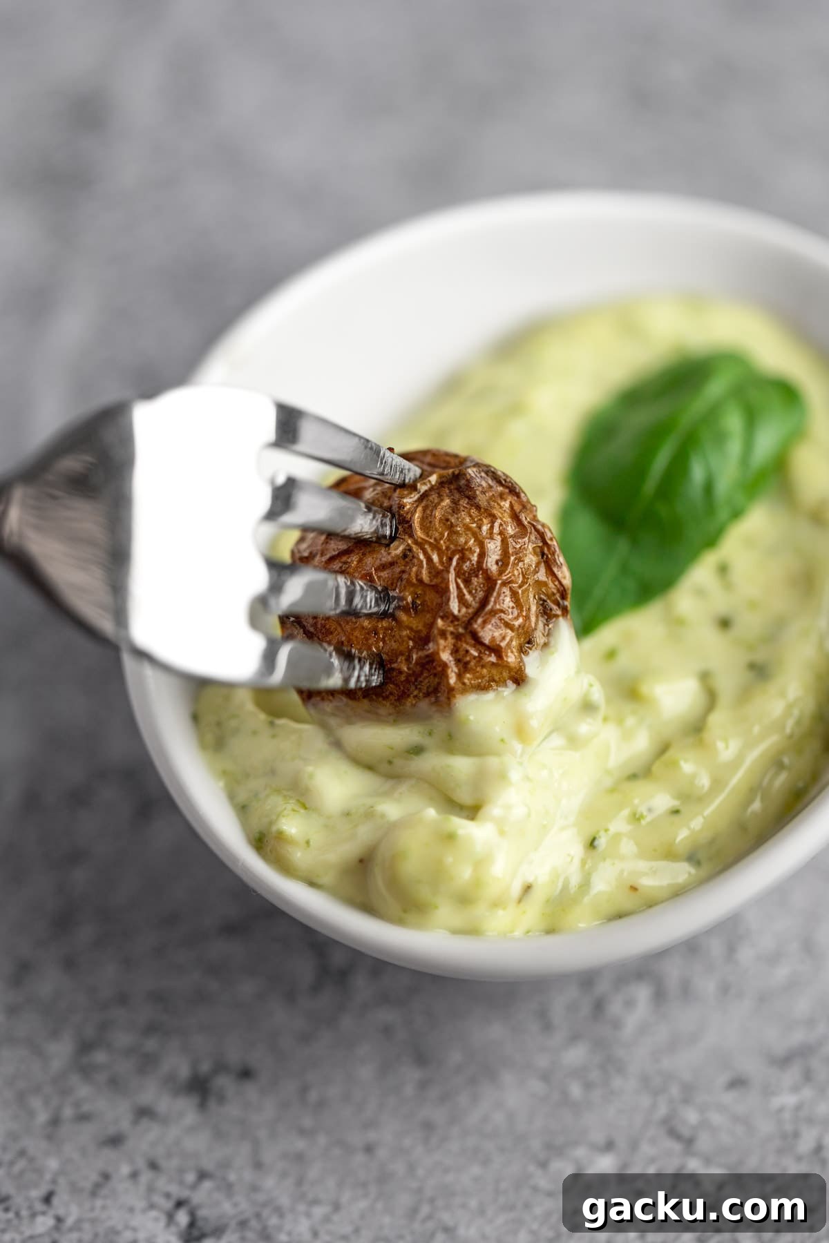 Creamy Pesto Aioli Recipe for Sandwiches & Dips 5 A fork dipping a home fry into a small white bowl of pesto aioli dip.