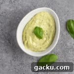Pesto aioli garnished with fresh basil leaves, on a grey marble table.