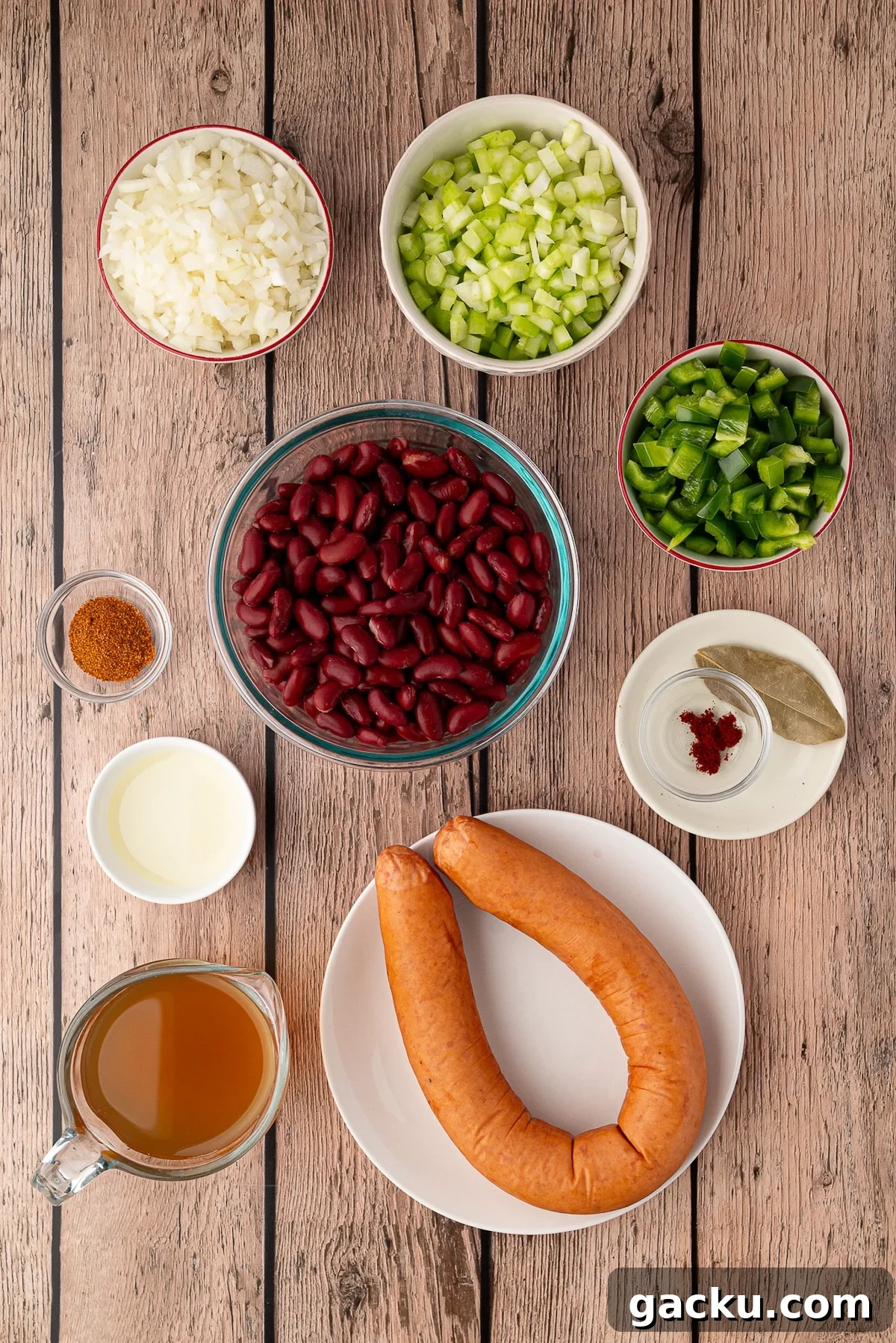 Ingredients for easy skillet red beans including canned kidney beans, H-E-B smoked sausage, diced onion, green bell pepper, celery, and Cajun spices arranged on a table.