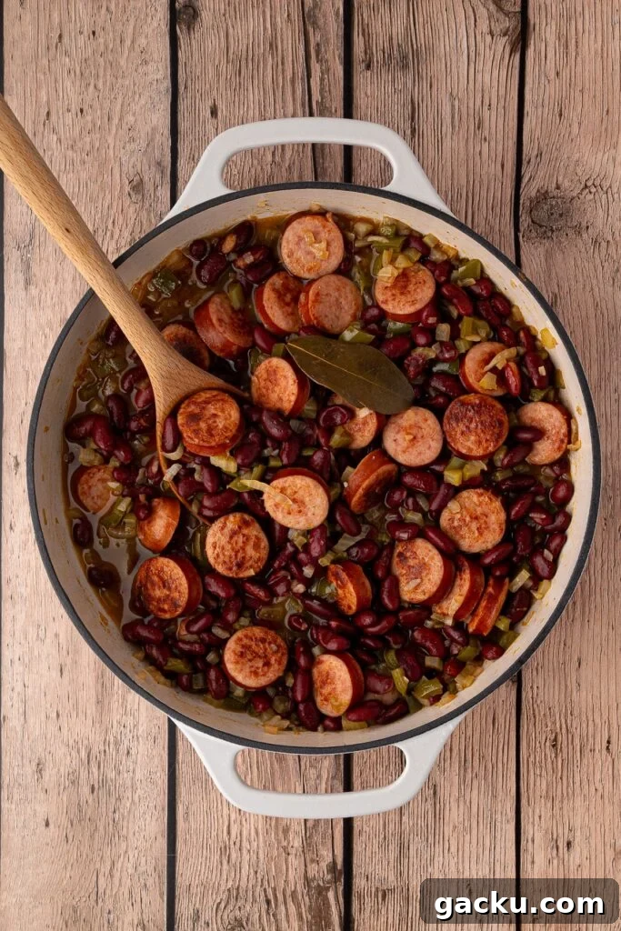 Canned kidney beans and chicken broth being added to the skillet with the sautéed vegetables and sausage.