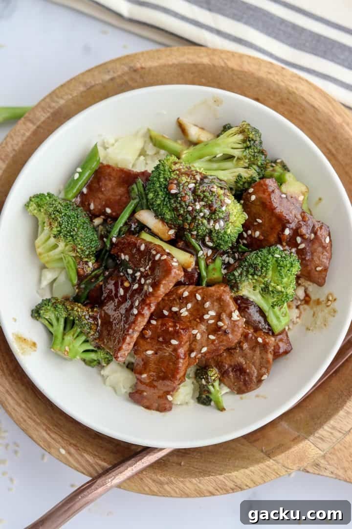 Mongolian beef served in a white bowl and garnished with extra Asian sauce and sesame seeds.